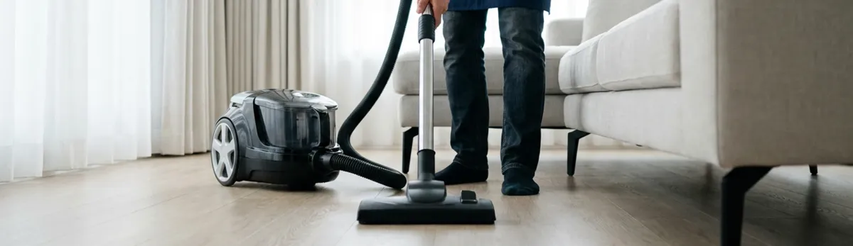 Professional house cleaner vacuuming a living room floor with a canister vacuum cleaner, Jackson, MI.