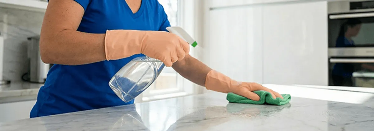 Maid service worker spraying and wiping a kitchen countertop with a microfiber cloth for sanitizing, Jackson, MI.